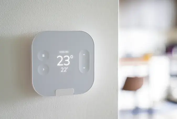 Modern smart thermostat on wall showing temperature and cooling mode